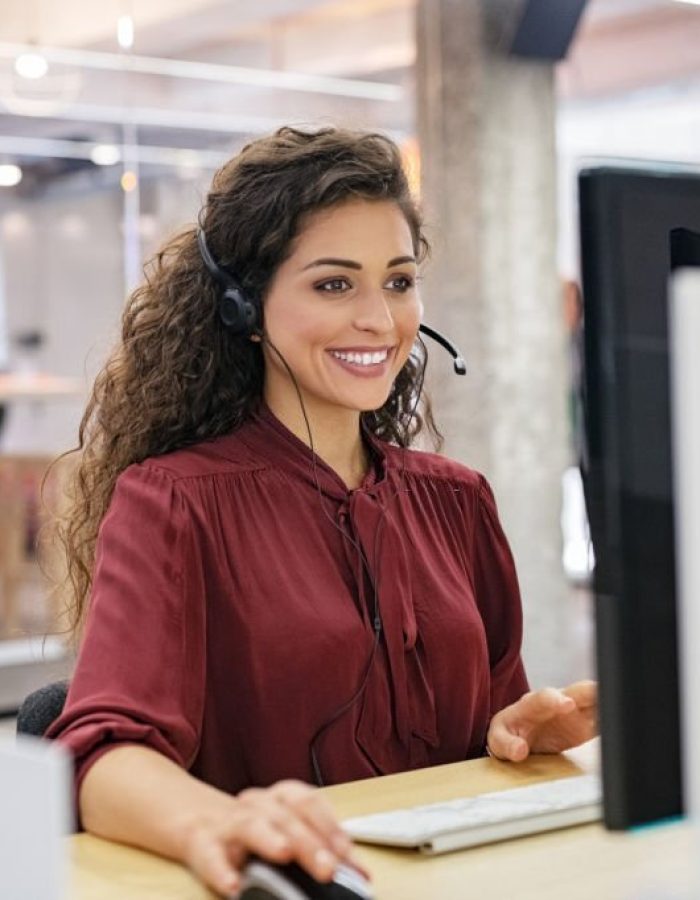 Customer support phone operator working at computer. Happy call center agent working on support hotline in office. Smiling call center agent in conversation with customer over headset.